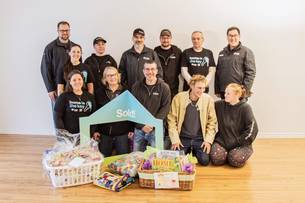 A group of Medicine Hat ReStore staff, Chapter volunteers and Habitat staff stand and kneel with new Habitat homeowners during a home possession in Medicine Hat. 