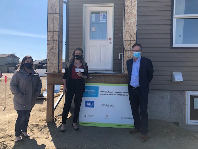Annette accepts a donation cheque in front an unfinished Medicine Hat Habitat home in 2020.