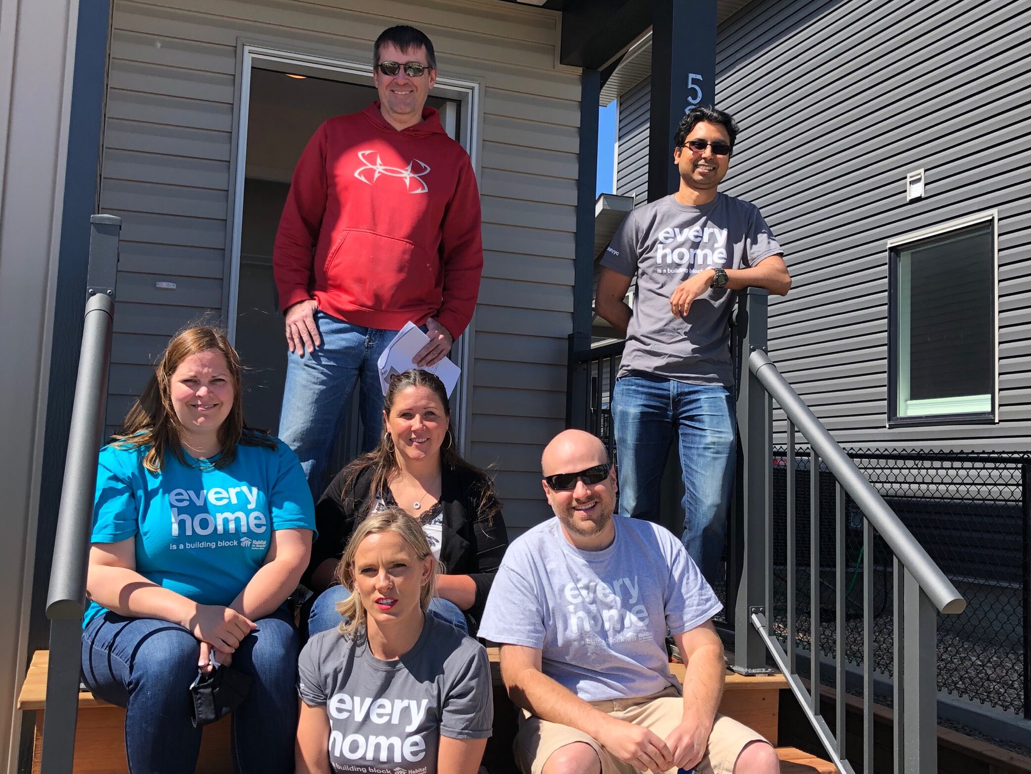Annette and five other Chapter volunteers sit together on the front steps of a completed Habitat home in Medicine hat. 
