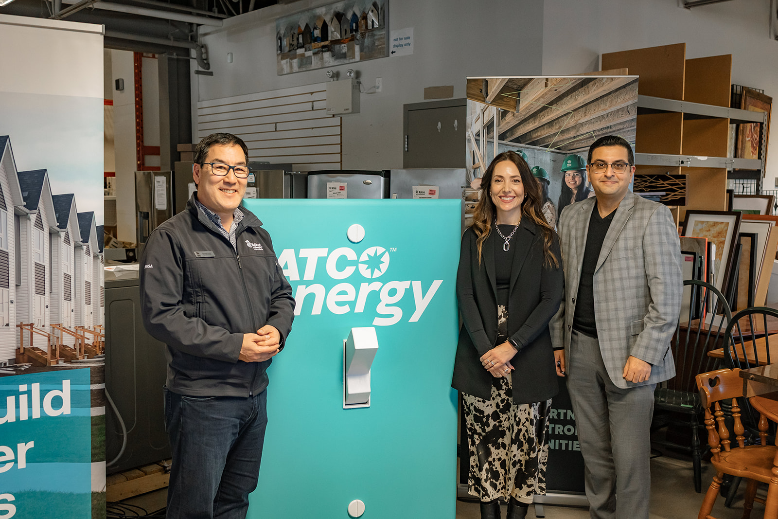 President and CEO of Habitat Southern Alberta stands with ATCO Energy's Lindsay Hagen and Neeraj Ghai beside a human-sized light switch with ATCO Energy branding.