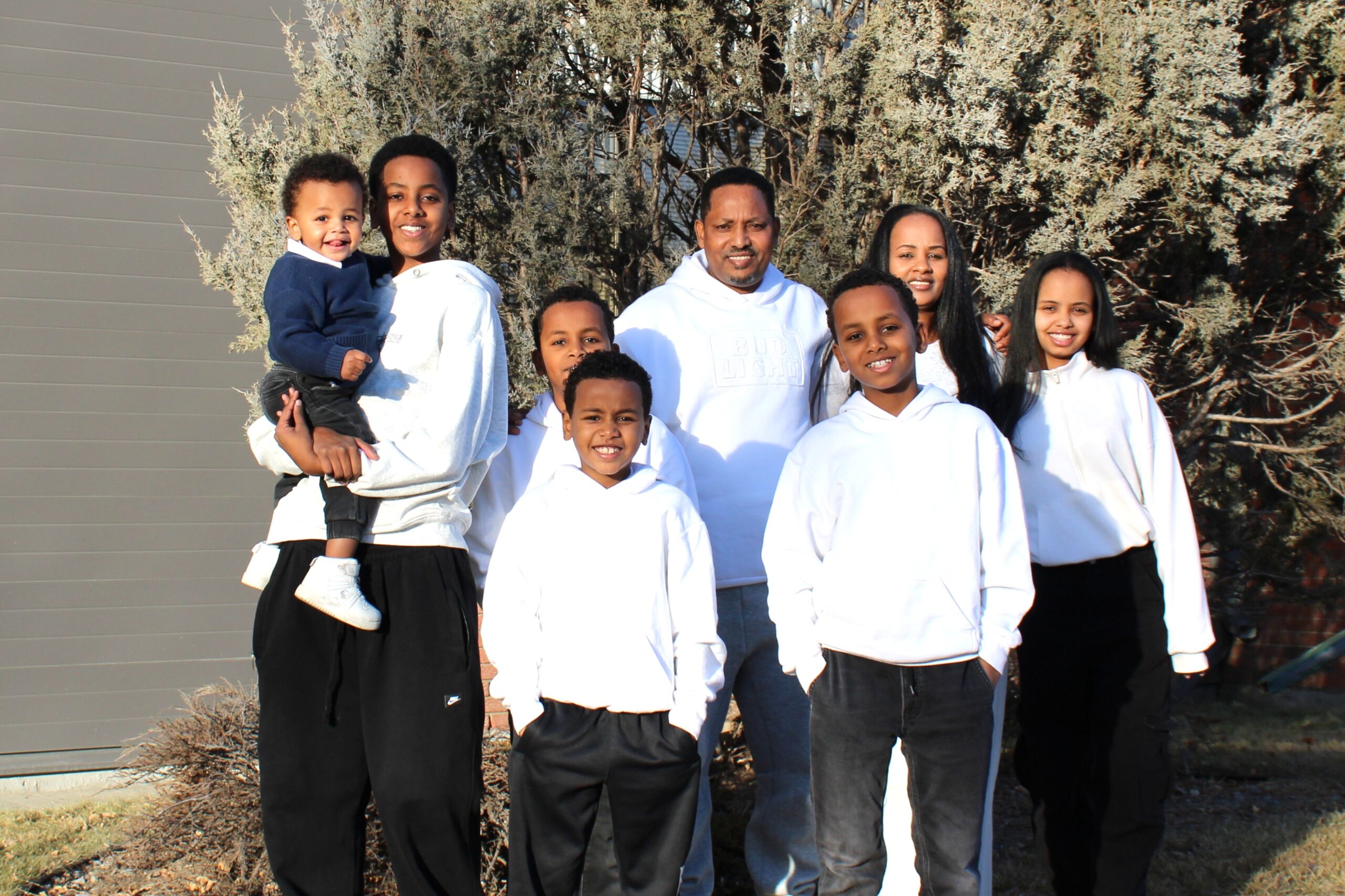 Gebremeskel and Asmerat stand with their children, ages 15 to 1, in matching white shirts and black pants.