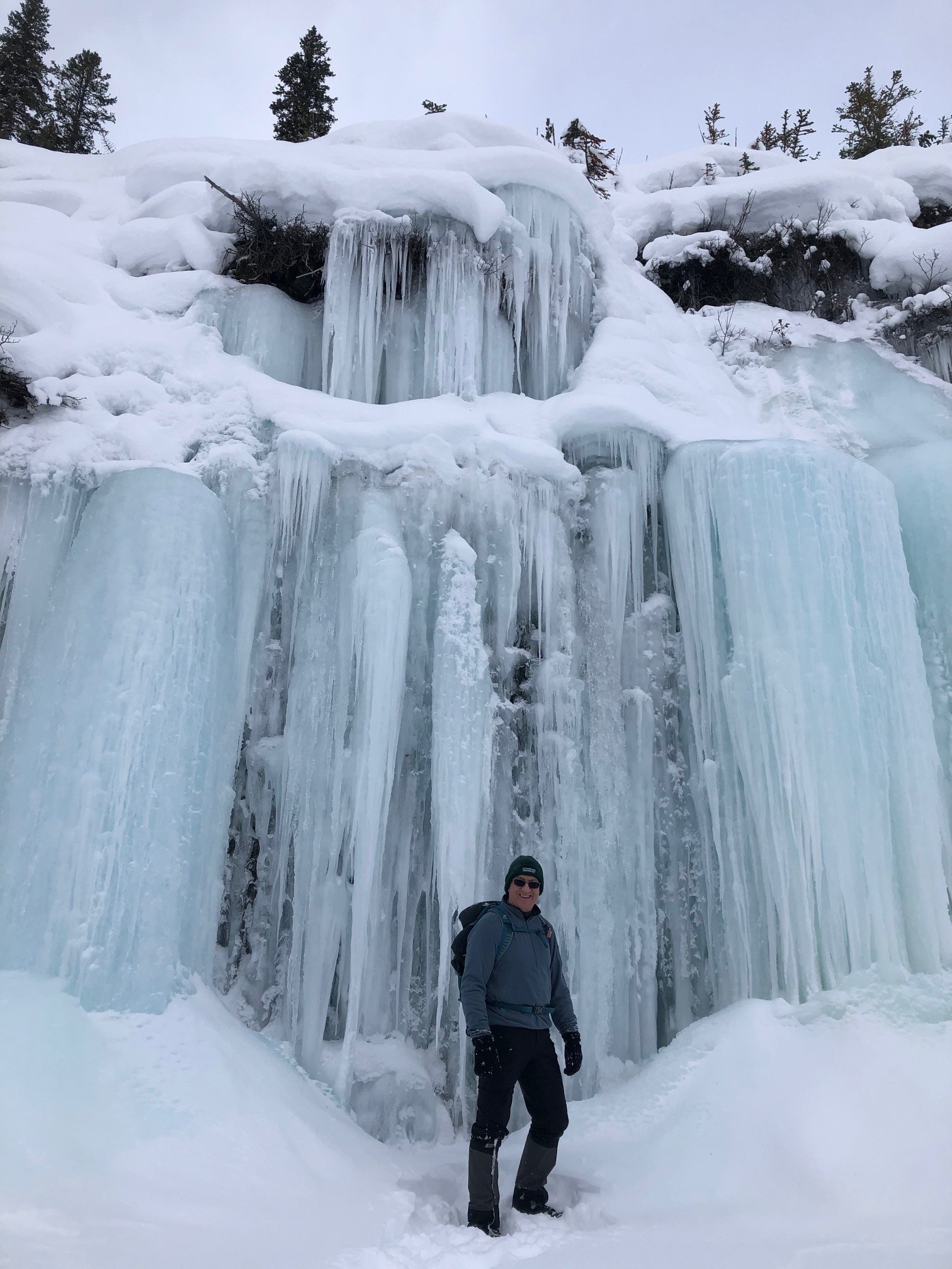 Steve stands under a frozen waterfall on a hike.