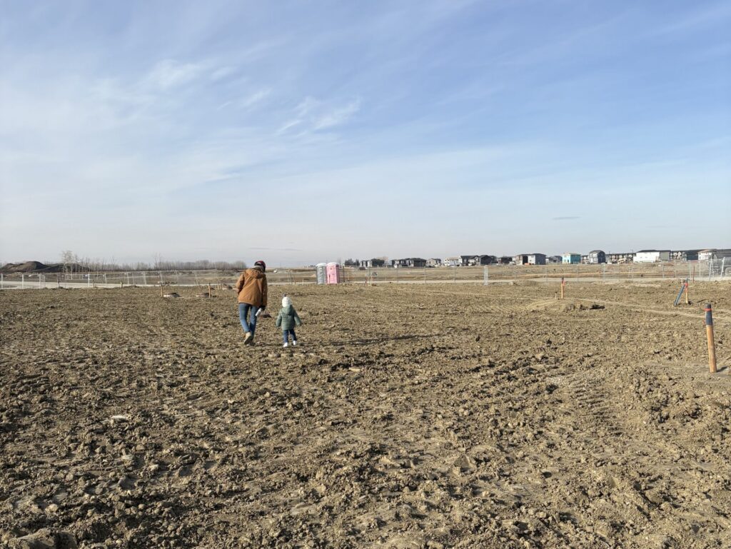 Three year old Adam walks with Site Supervisor Trish on the dirt land where his future home will be. 