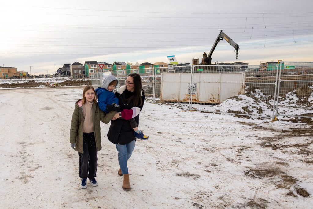 Chantelle, Emma and Jaxon walk on a snowy street with a crane lifting forms in the background.