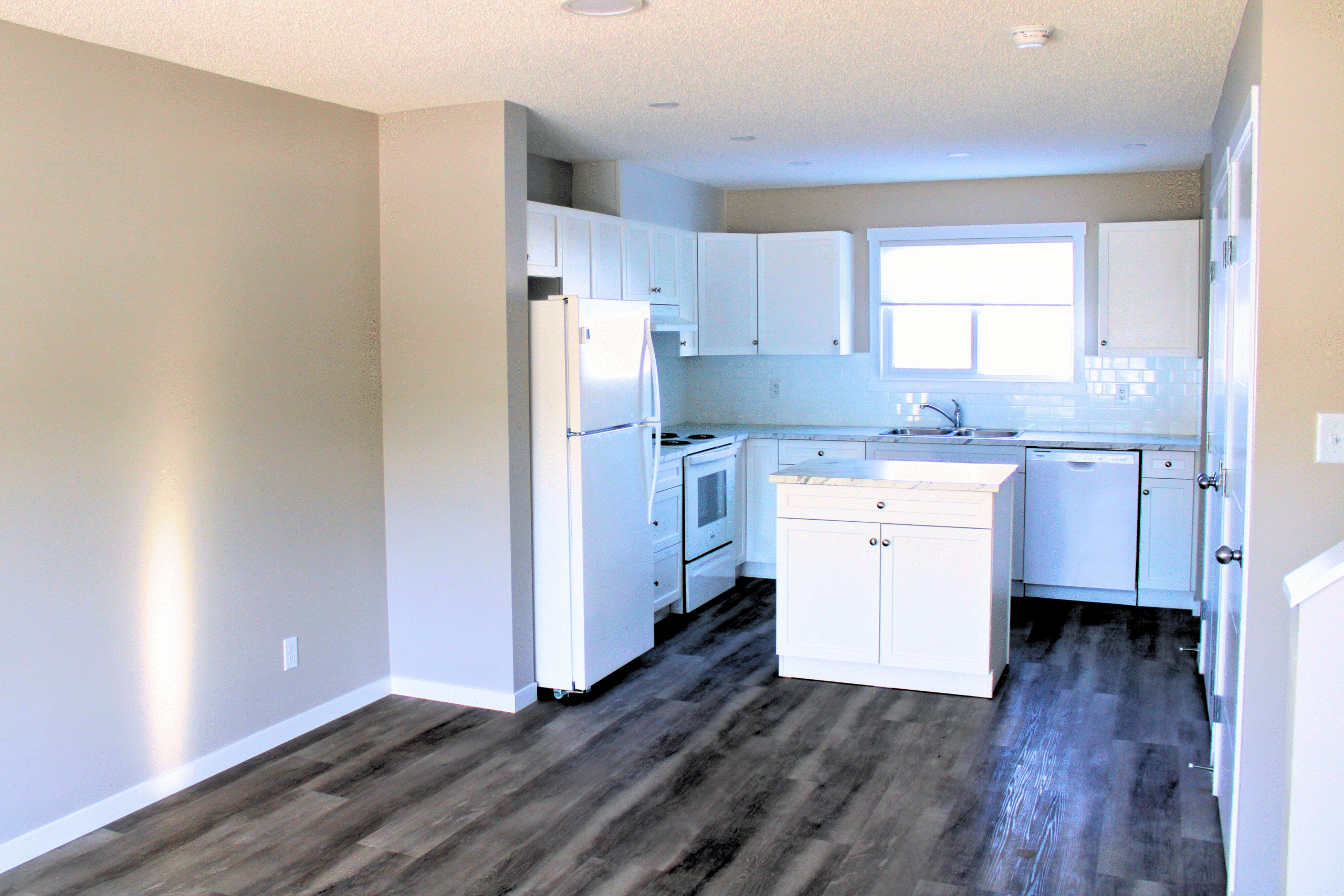 An all white kitchen and beige walls in an empty main floor of a home.