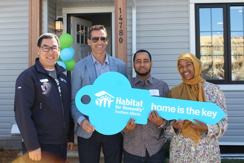 Habitat's CEO and Sterling Homes' VP stand with future homeowners holding a large key cutout that reads Home is the key.