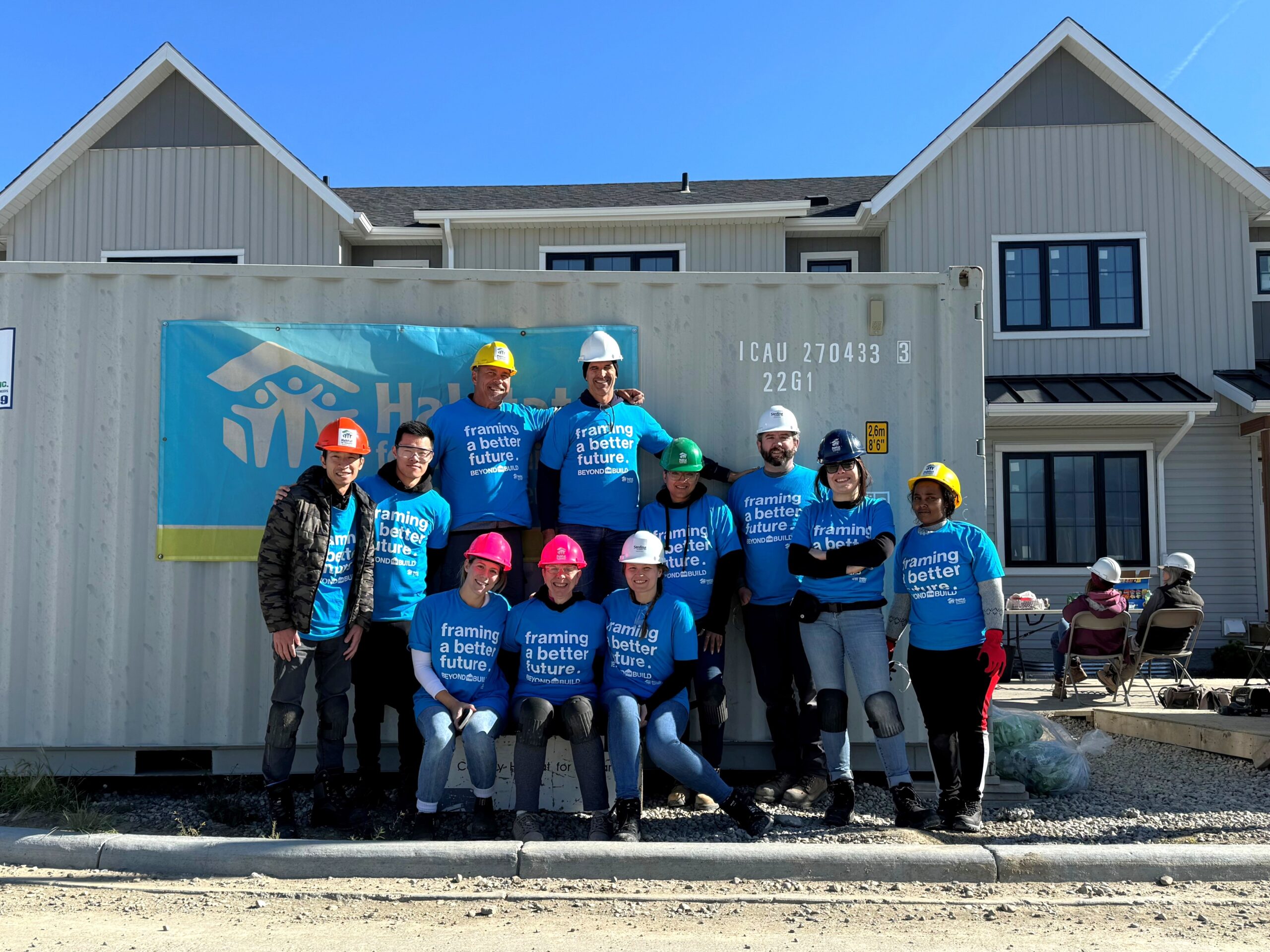 Sterling Homes employees wearing matching blue Habitat tshirts in front of a seacan and finished Habitat homes.