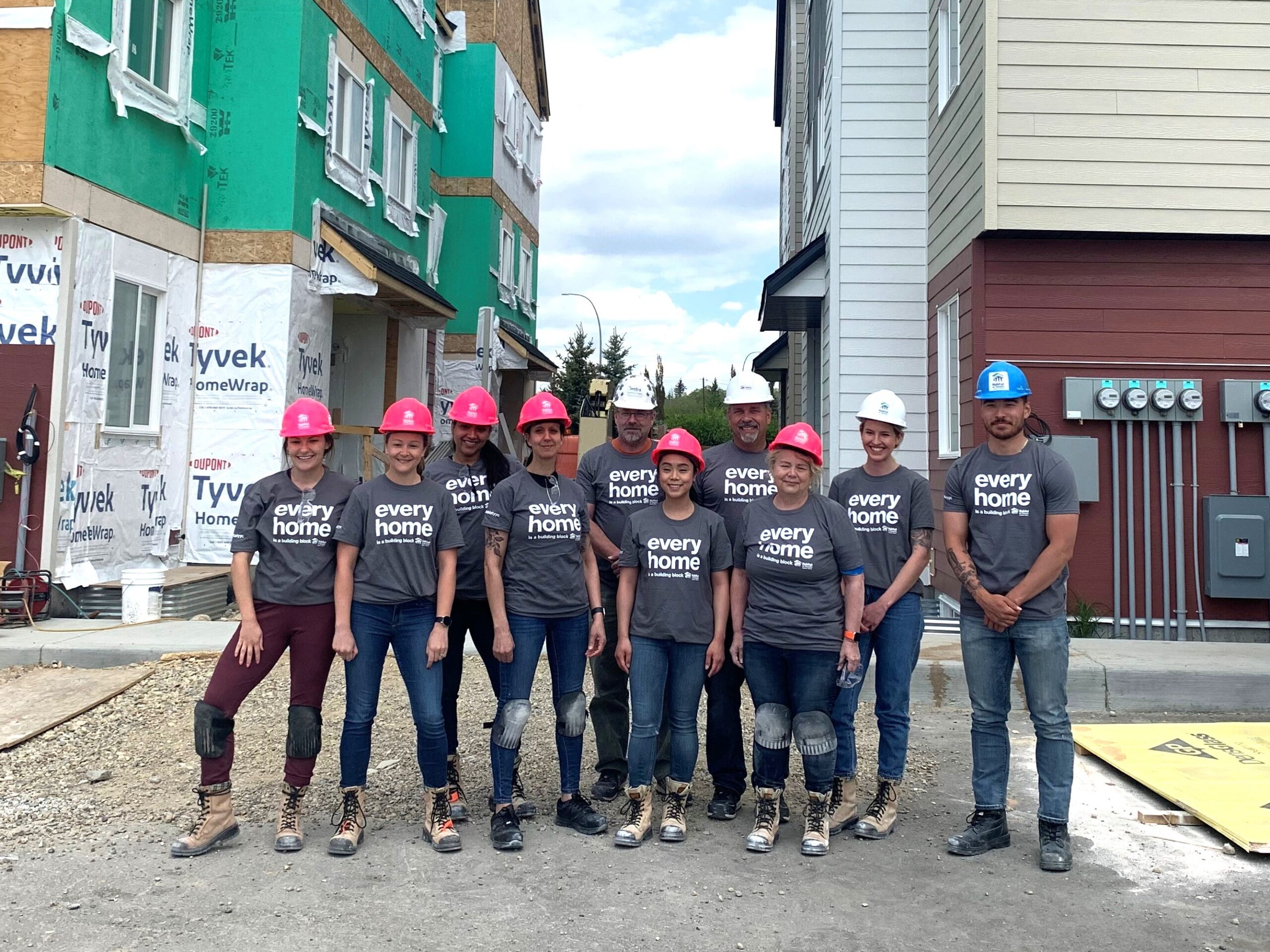 A group of Sterling Homes staff wearing grey Habitat tshirts and pink hardhats.