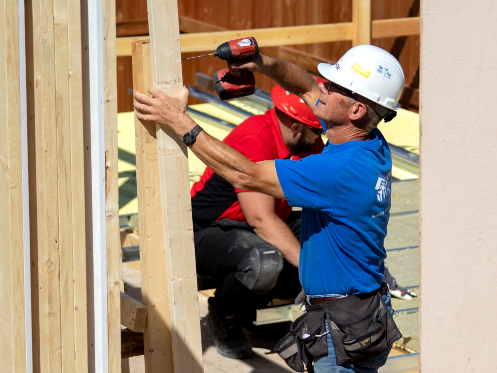 Byron operates a drill while building an exterior wall.