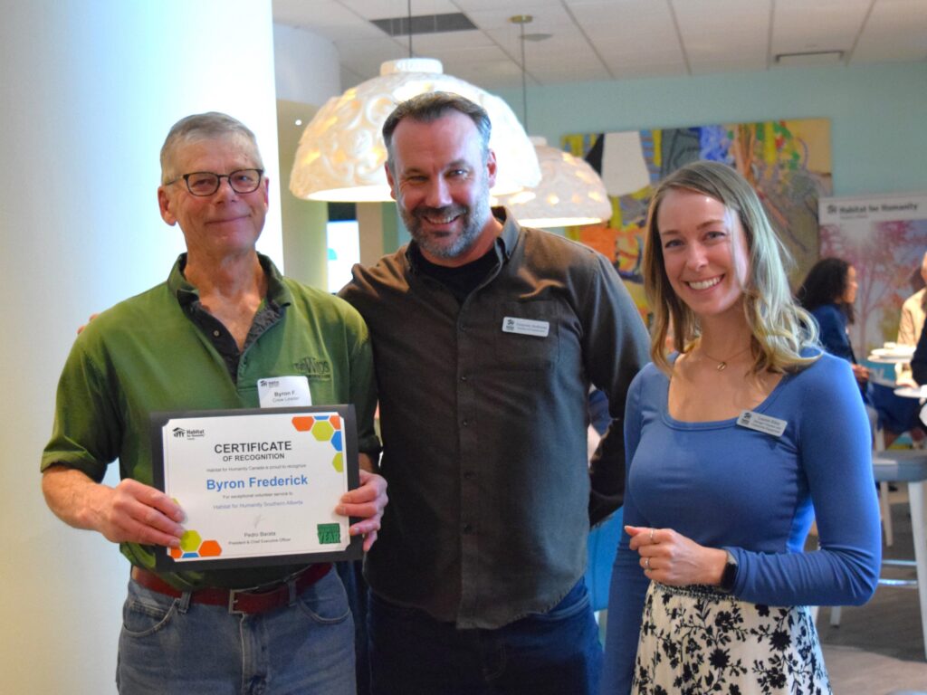 Byron holds his award certificate from Habitat Canada alongside two Habitat staff.
