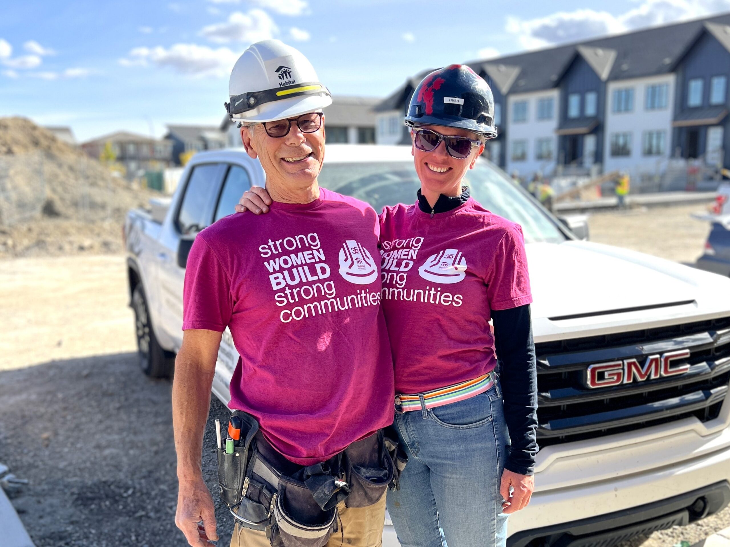 Byron and Trish wearing pink Women Build Stronger Communities tshirts with a construction site behind.