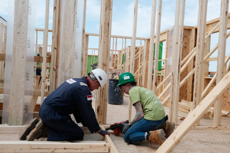 Two Habitat volunteers work together framing an interior wall with lumber.
