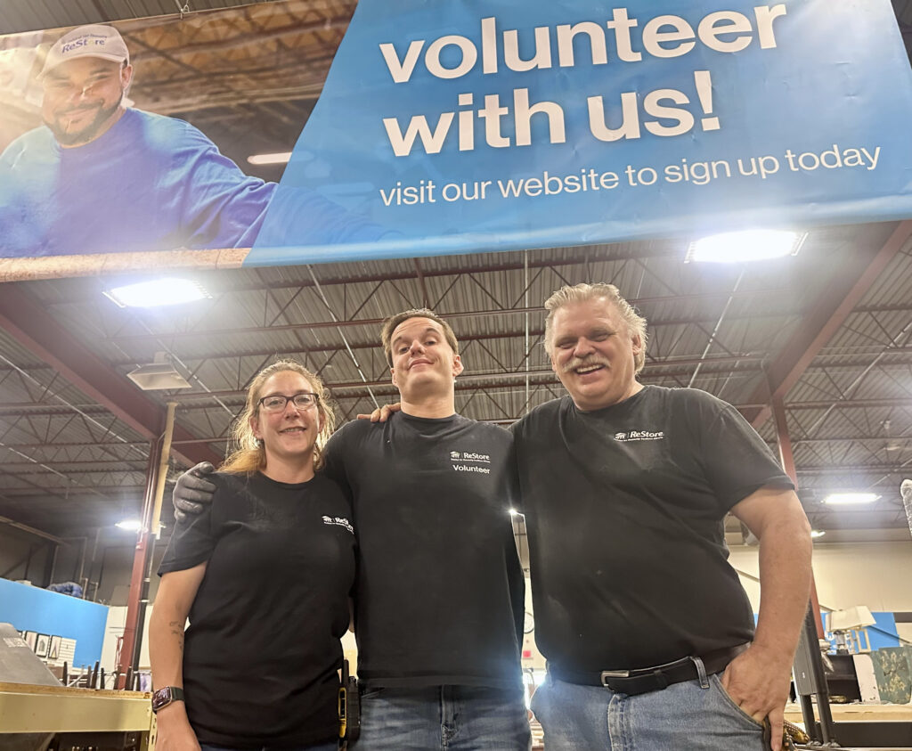 Sarah, Joe, and JP stand under a volunteer with us banner