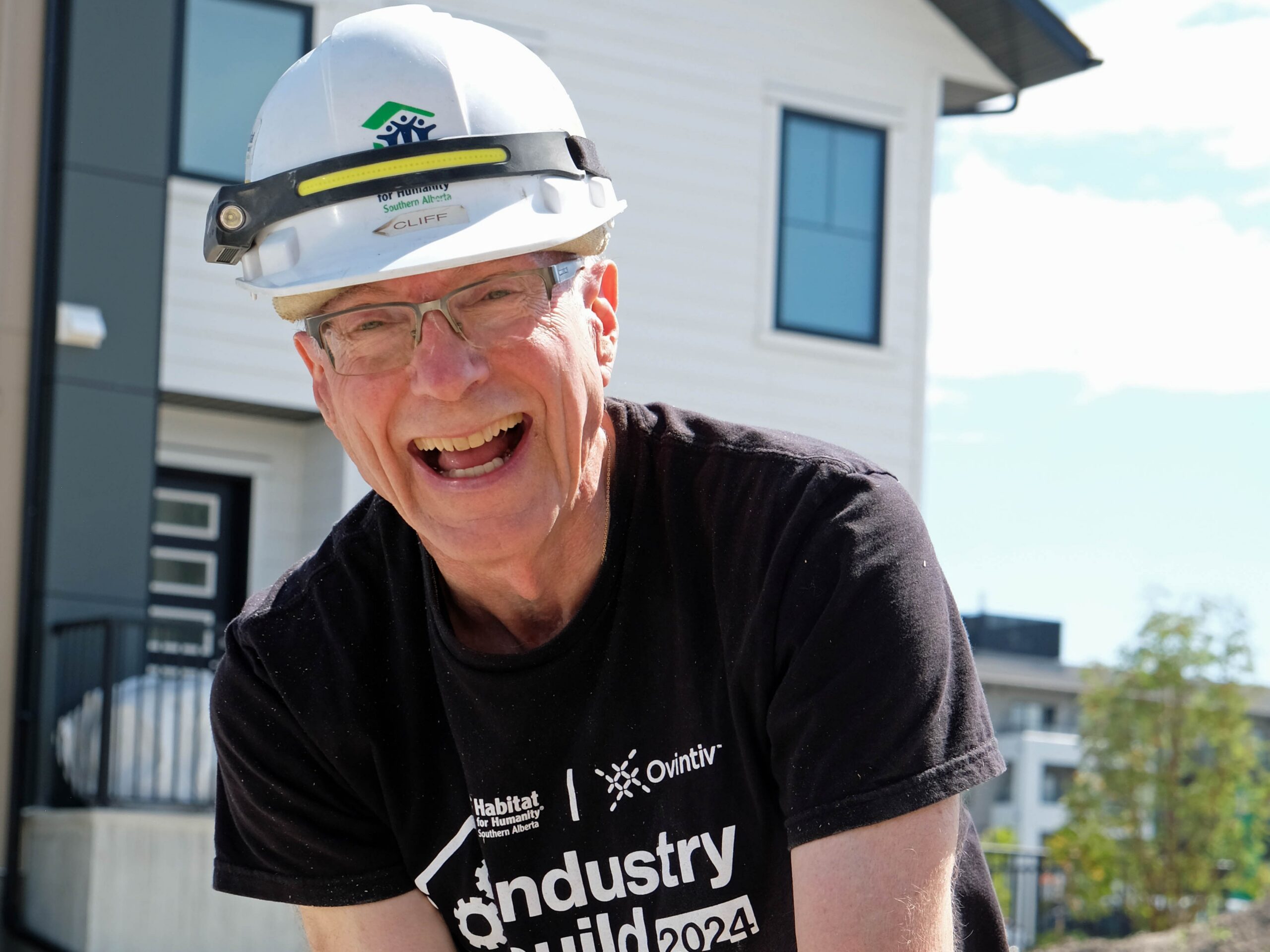 A man wearing a white hard hat smiles big.