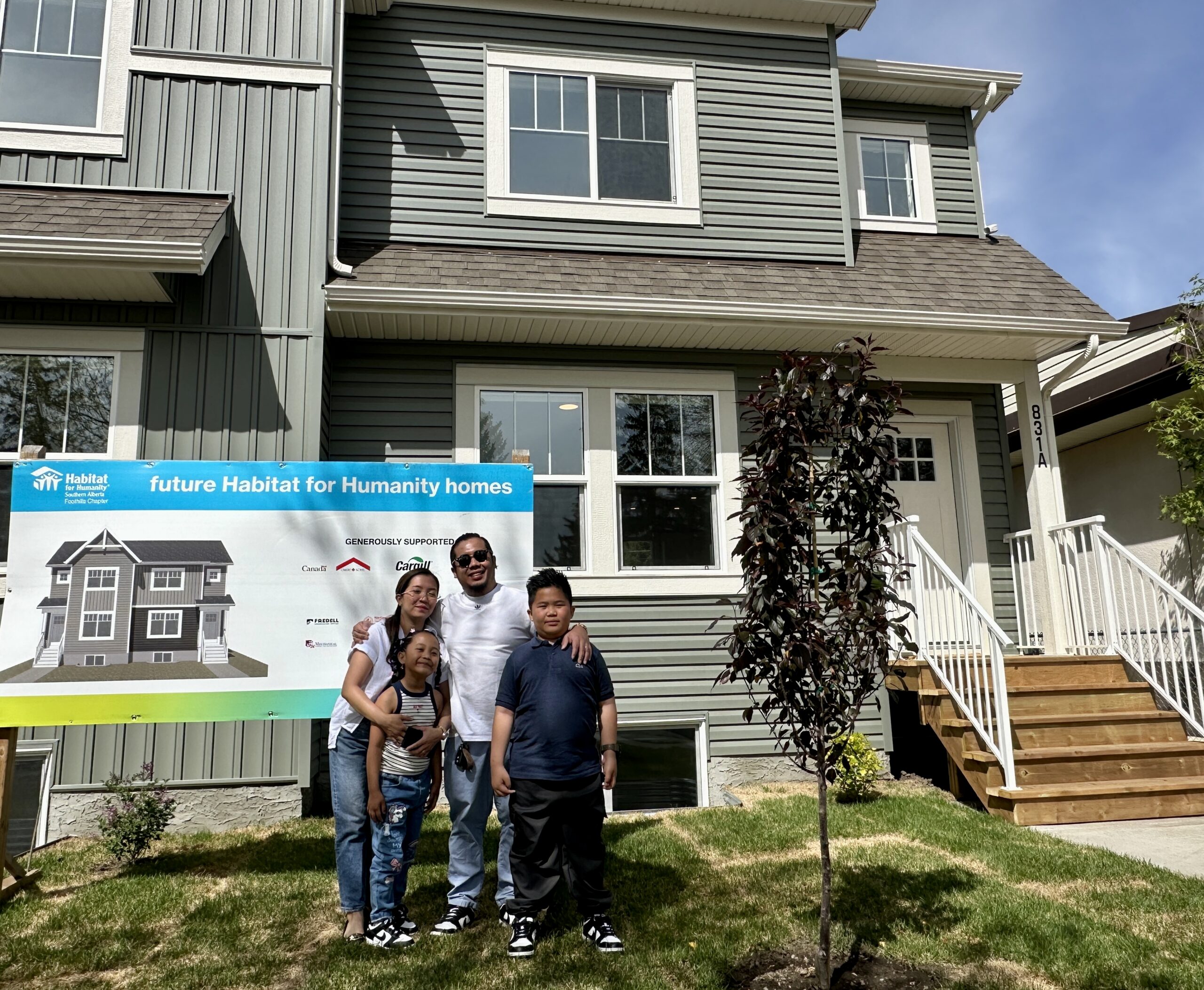 A family of four stands in front of their house.