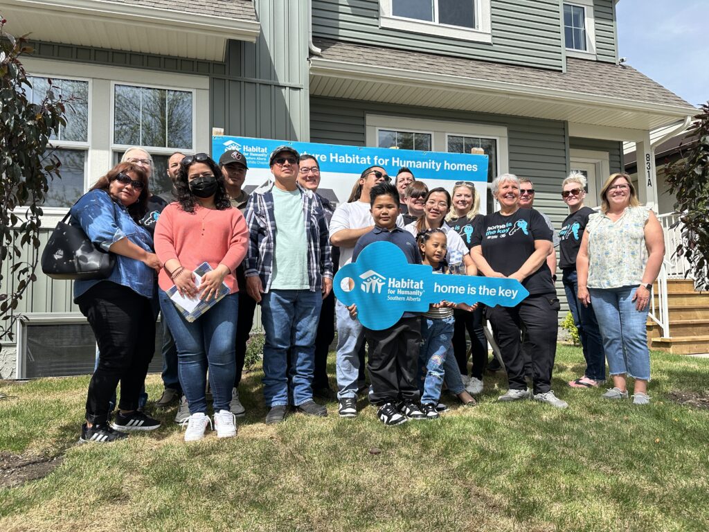 A group of people stand together on the front lawn of a duplex.