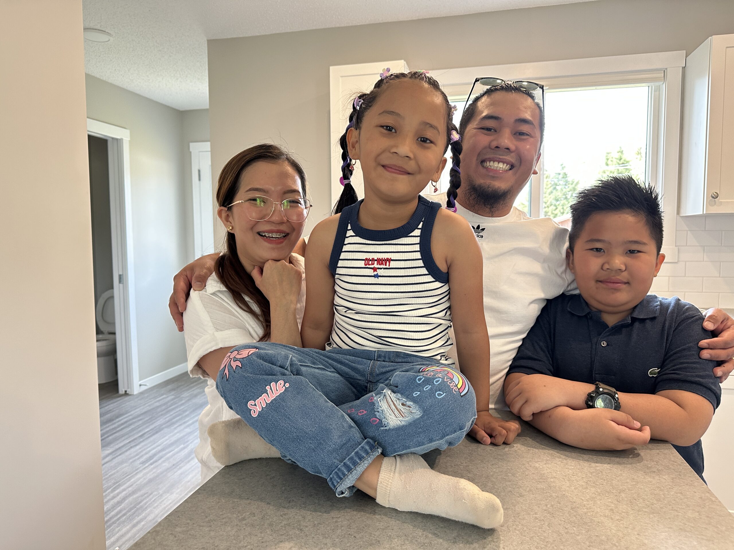 A family of four surrounds a kitchen island.