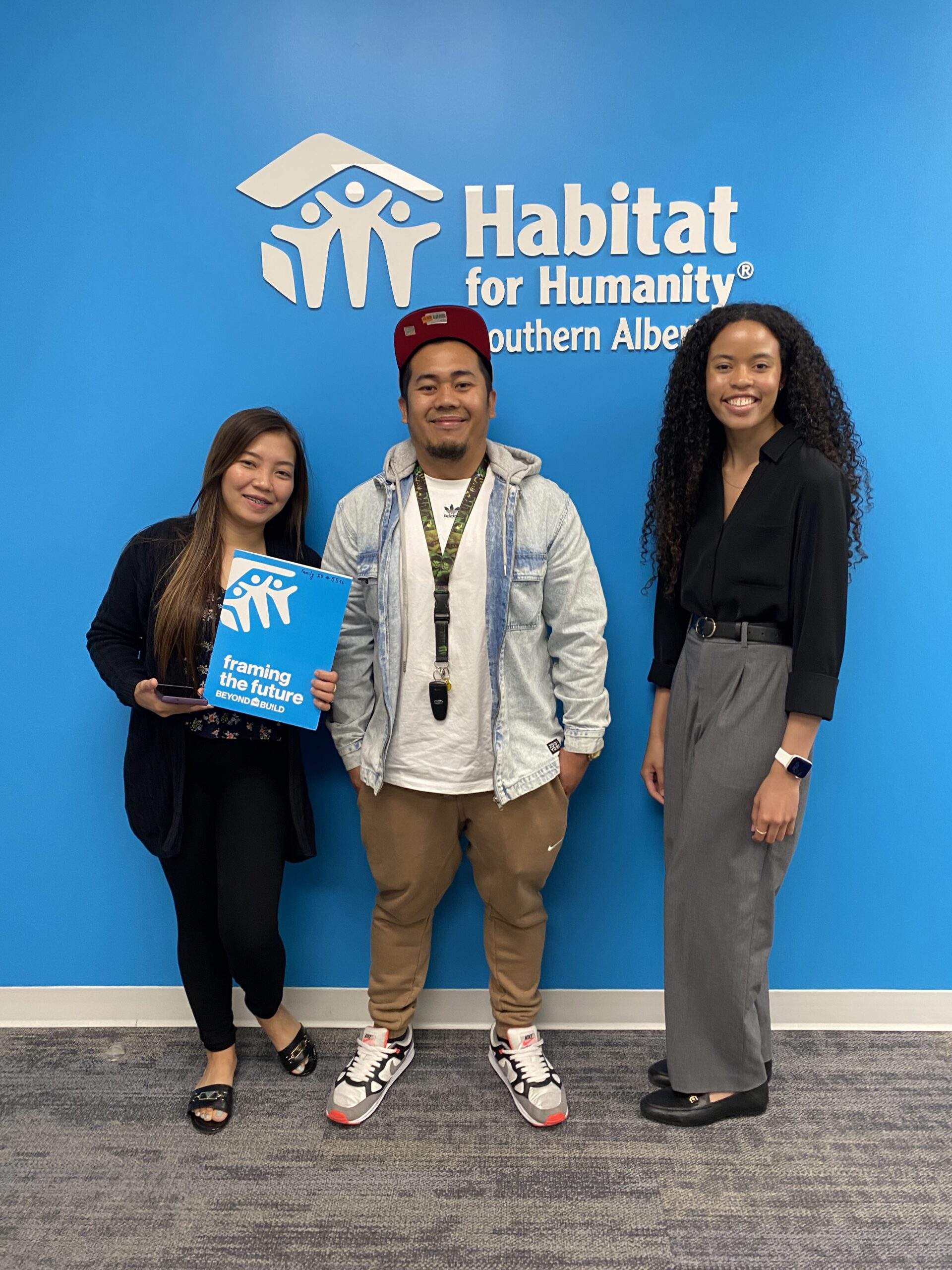 Three people stand in front of a blue wall.