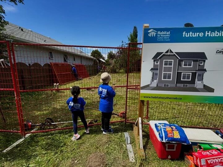 Two small kids look through a fence at an empty lot.