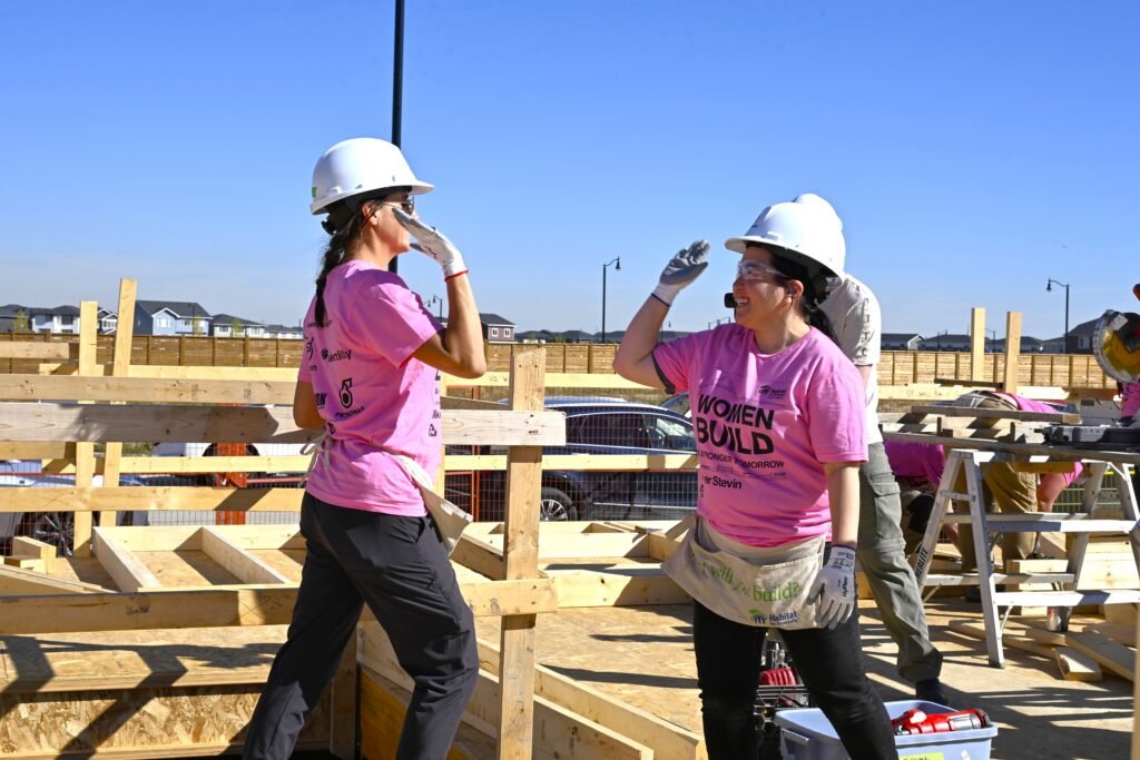 Two women in pink hard hats high-fiving on a Habitat build site during Women Build