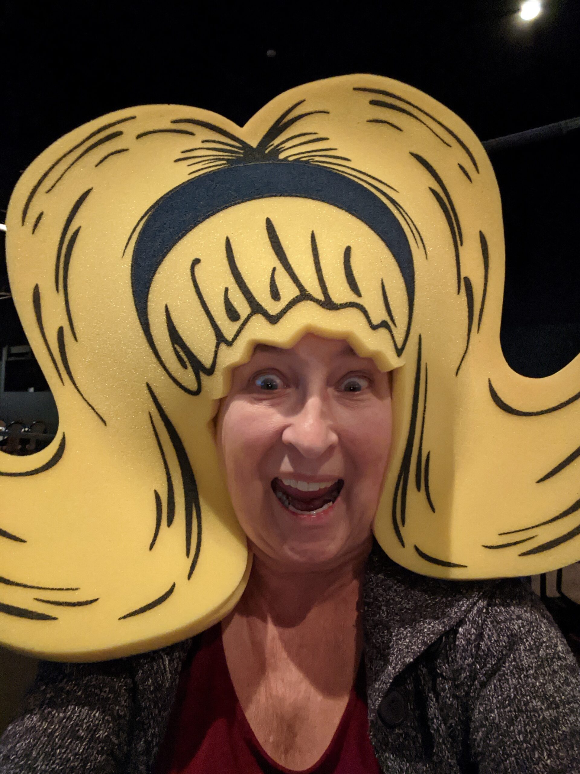 Marie wears a big yellow foam hat that looks like a wig.