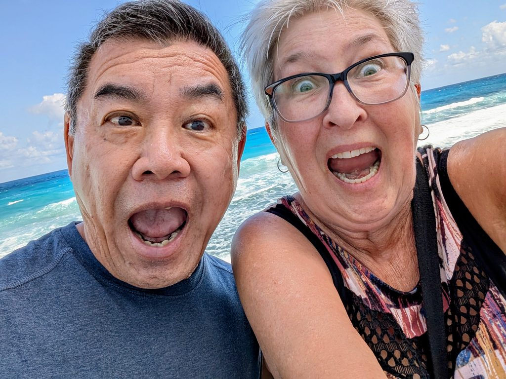 Marie and her husband smile animatedly on a beach.